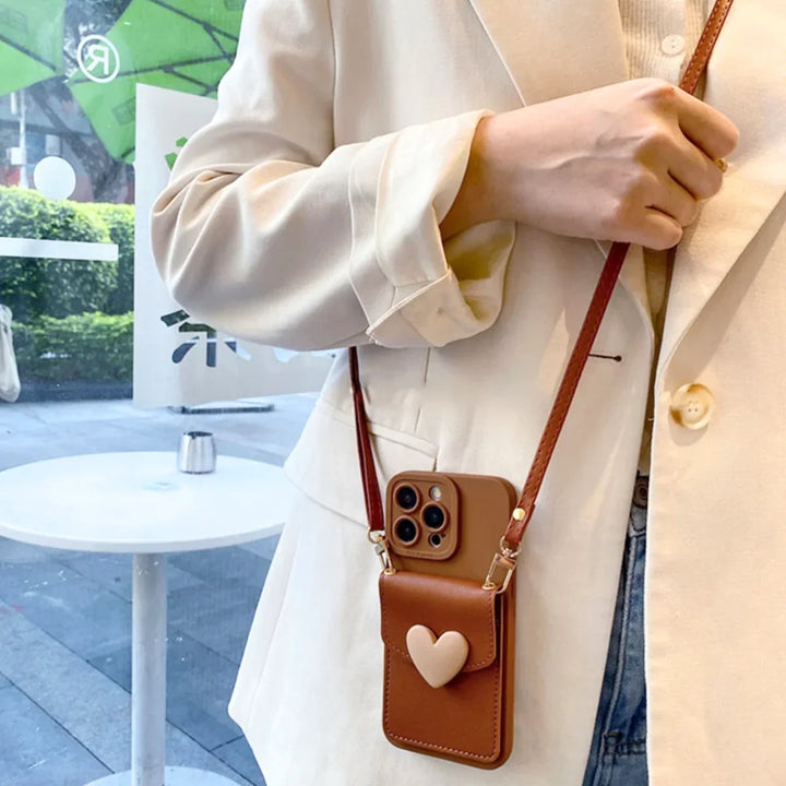 A person in a cream blazer holds a brown purse with a chic phone case and beige heart design, standing indoors near a window with greenery and outdoor seating visible outside.