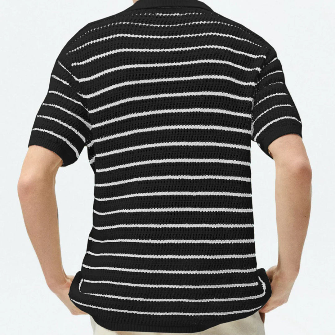 A person wearing a black retro knit polo with white horizontal stripes, shown from the back, hands resting on their hips.