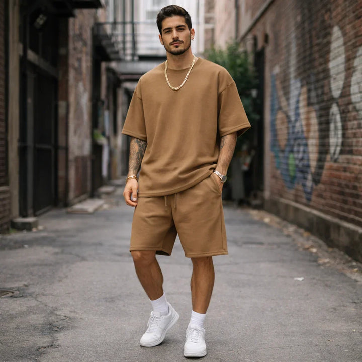 Man in tan casual short set with gold chain and white sneakers, urban backdrop, Rovelli fashion
