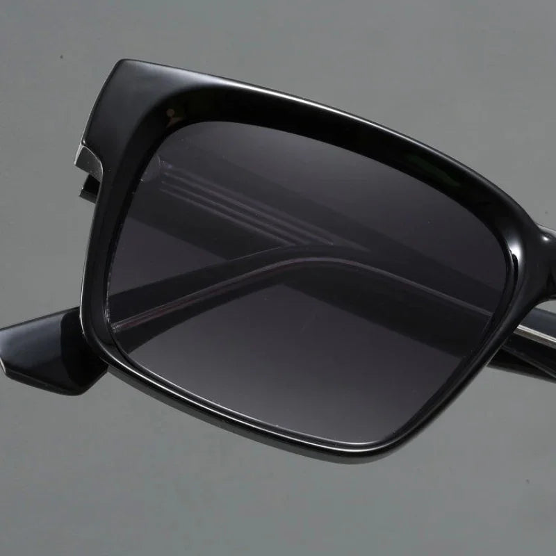 Close-up of black rectangular sunglasses with modern design and dark tinted lenses, crafted with durable frames and UV400 protection, shown against a plain gray background.