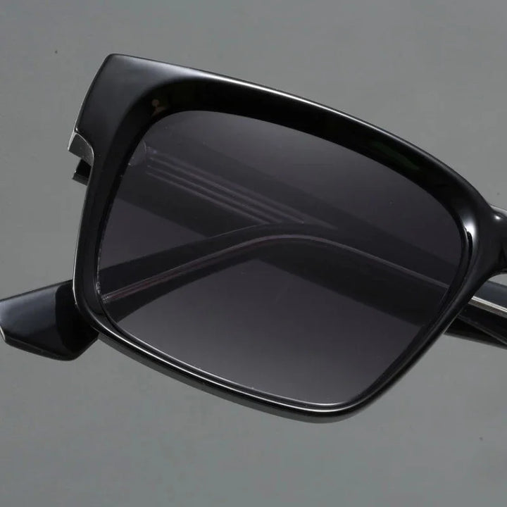 Close-up of black rectangular sunglasses with modern design and dark tinted lenses, crafted with durable frames and UV400 protection, shown against a plain gray background.