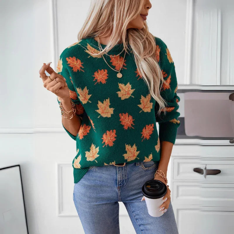 A woman with long blonde hair wears a green comfortable sweater with a maple leaf pattern, blue jeans, and gold jewelry. She holds a coffee cup in one hand and a cigarette in the other, standing in a white kitchen.