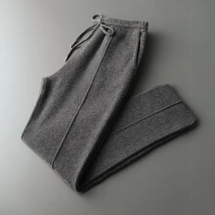 A pair of folded, dark gray comfortable pants with a drawstring waistband and visible seam lines, featuring durable construction, displayed on a plain gray background.