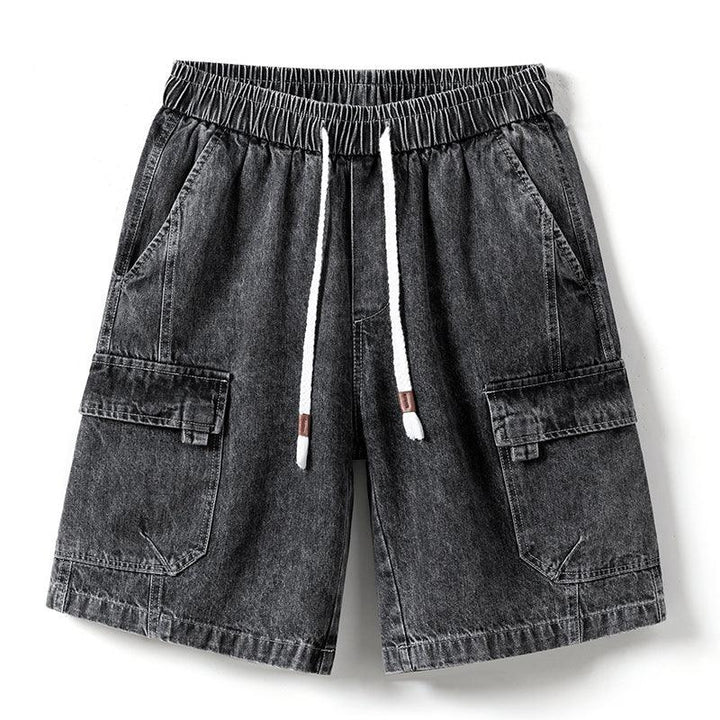 A pair of mens denim shorts in black with an elastic waist, white drawstring, side pockets, and flap pockets on each leg—laid flat on a white background.