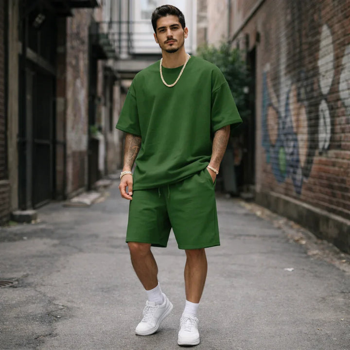 Man wearing green oversized T-shirt and shorts from Rovelli, standing in urban alley