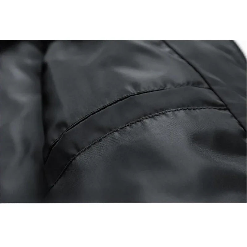 Close-up of a black, shiny, padded slim-fit jacket showing a seam and part of a pocket, highlighting the smooth and slightly reflective fabric texture with wind-resistant features.