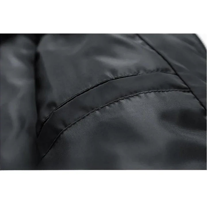 Close-up of a black, shiny, padded slim-fit jacket showing a seam and part of a pocket, highlighting the smooth and slightly reflective fabric texture with wind-resistant features.