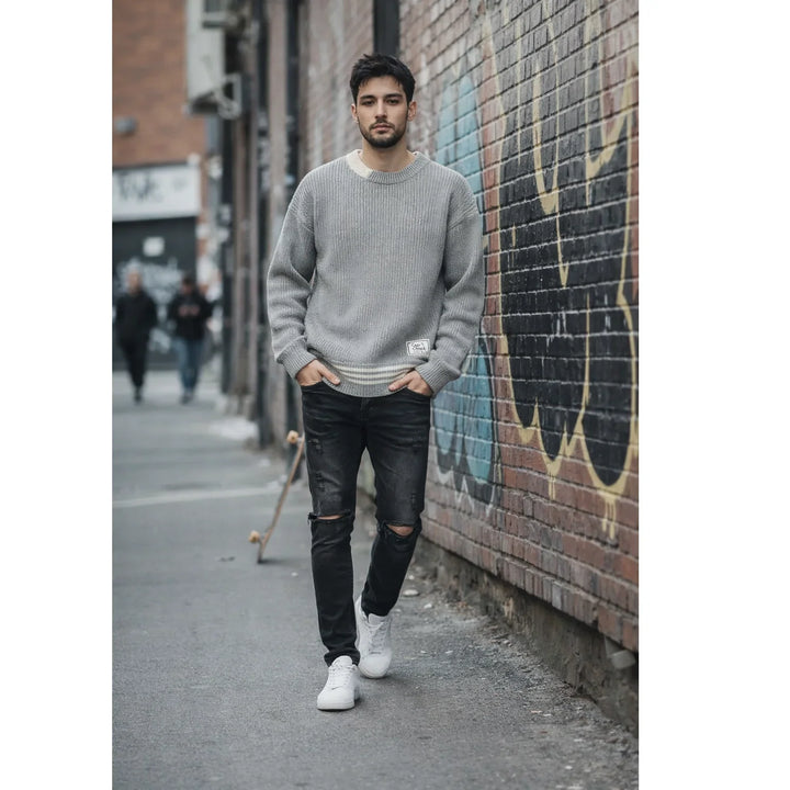 Man in grey sweater and ripped black jeans walking in urban alley with graffiti wall, Rovelli fashion
