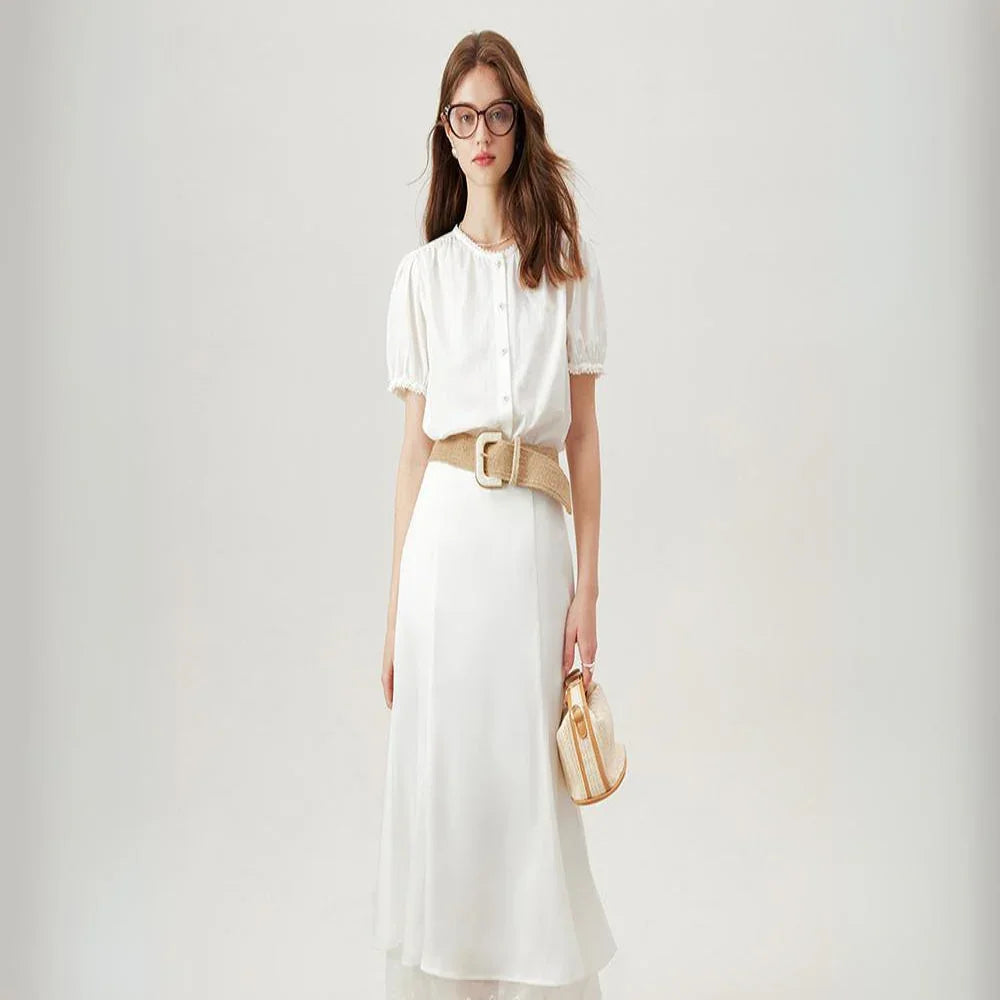 A woman wearing a white short-sleeve dress with a beige belt, holding a small round handbag. Her look is effortlessly chic—perfect for pairing with a versatile blouse or button-up blouse for added style options.