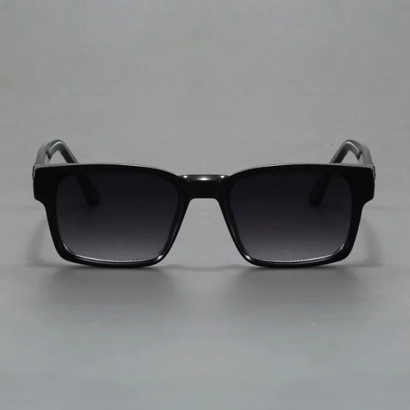 A pair of black square-framed sunglasses with durable frames and dark tinted lenses, featuring modern design and UV400 protection, displayed against a plain grey background.