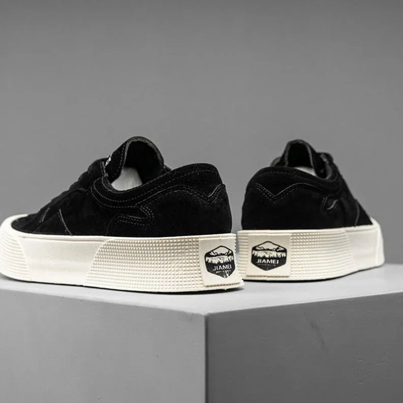 A pair of black suede lace-up sneakers with thick white soles and a JIAMEI label on the heel, featuring comfortable cushioning, displayed on a gray platform against a plain gray background.