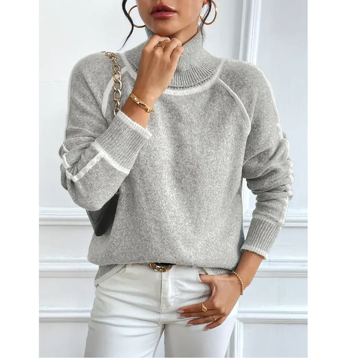 Woman wearing a grey turtleneck sweater and white pants, accessorized with gold jewelry from Rovelli