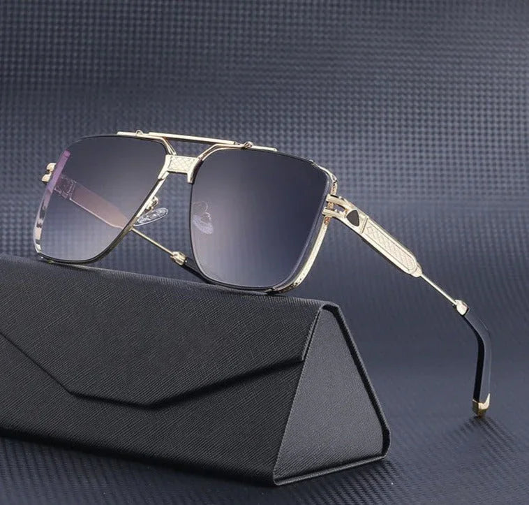 A pair of gold-framed vintage aviator sunglasses with dark gradient lenses and UV400 protection rests on a black, textured eyeglass case against a dark grey, patterned background.