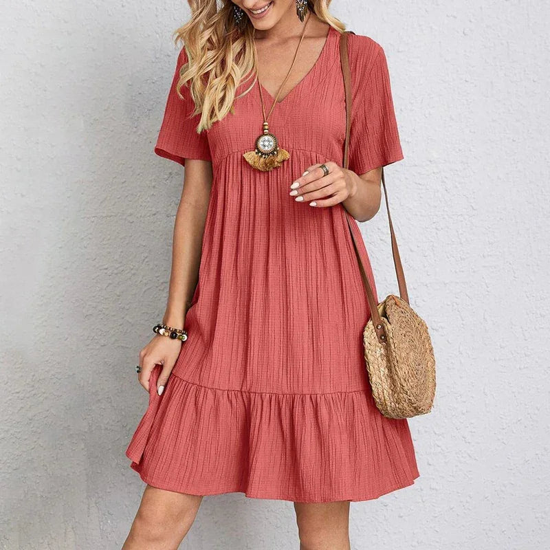 Woman wearing a casual pink short sleeve dress with ruffle hem and straw crossbody bag