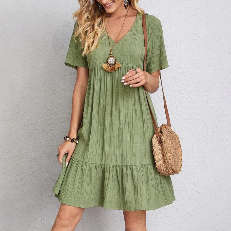 Woman in short sleeve green dress with v-neckline, straw bag, and boho necklace, Rovelli fashion