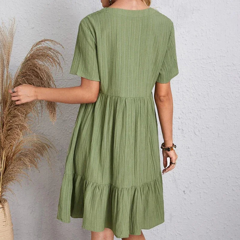 Woman wearing a loose green short-sleeve dress from Rovelli, standing by pampas grass.