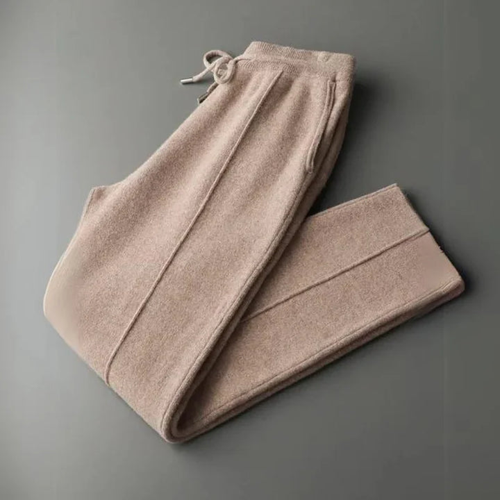 A pair of light beige, comfortable pants with a drawstring waistband and side pockets, featuring durable construction, neatly folded on a plain gray background.