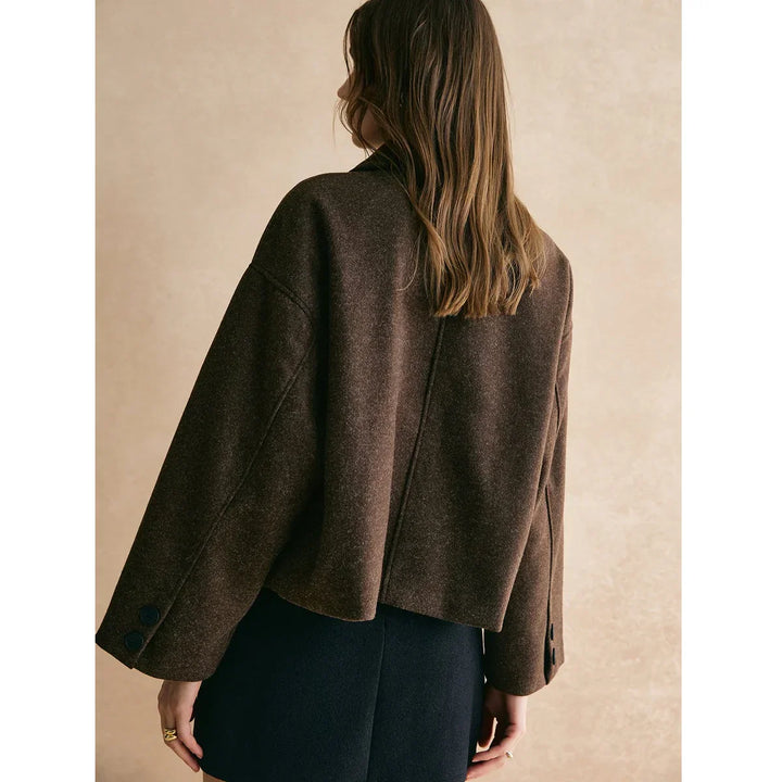 Woman wearing a cropped brown wool jacket from Rovelli, standing against a beige background