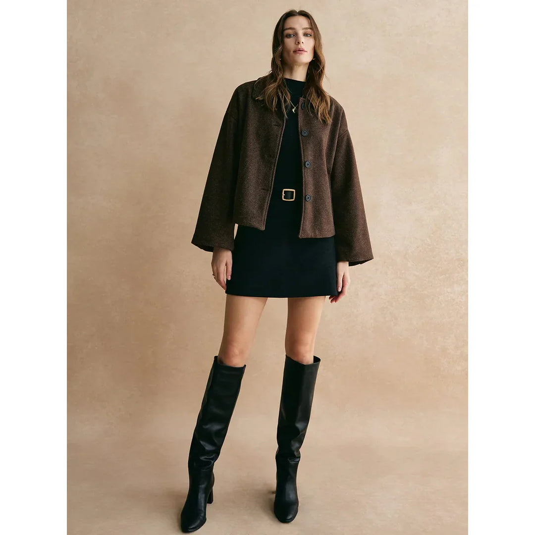 Woman modeling a brown jacket, black mini dress, and knee-high boots for Rovelli fashion