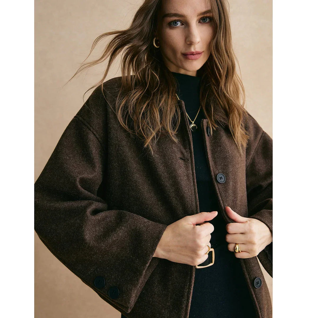 Woman wearing dark brown buttoned coat, gold jewelry, and black top, Rovelli fashion