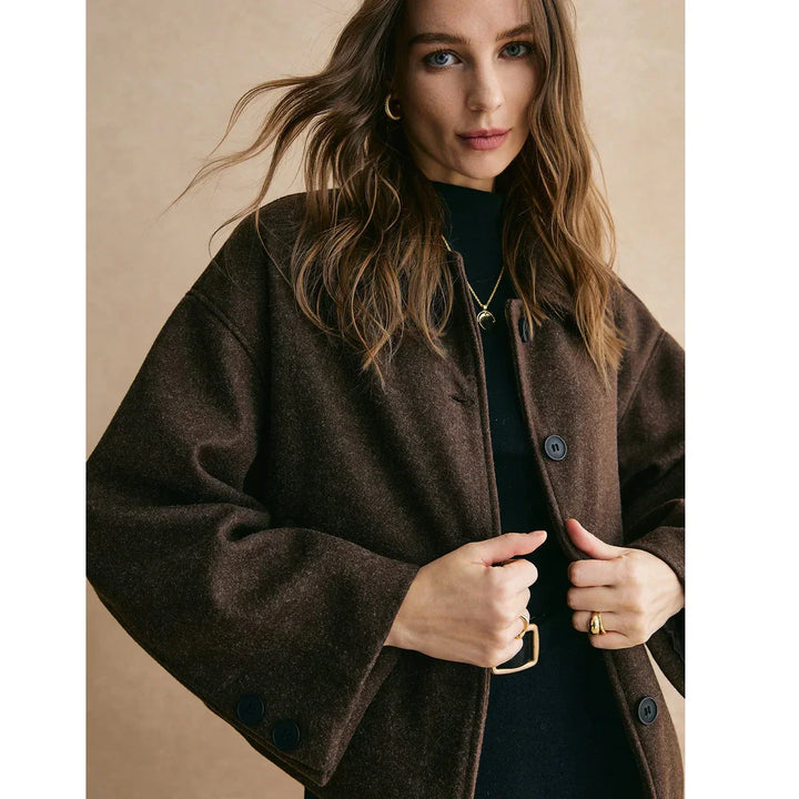 Woman wearing dark brown buttoned coat, gold jewelry, and black top, Rovelli fashion