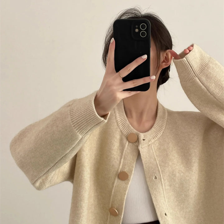 Woman in beige knit cardigan with gold buttons taking mirror selfie for Rovelli