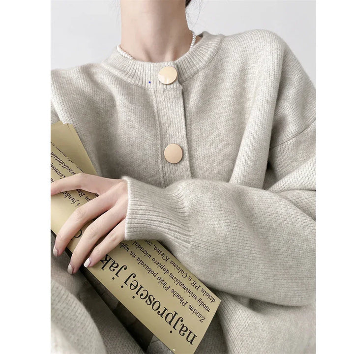 Woman in beige knit sweater with large buttons holding book, Rovelli fashion style