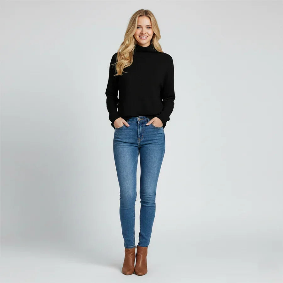 Woman in black turtleneck sweater, blue jeans, brown boots, standing studio Rovelli
