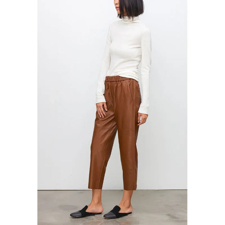 Woman wearing brown genuine leather pants from Rovelli, styled with white turtleneck top.