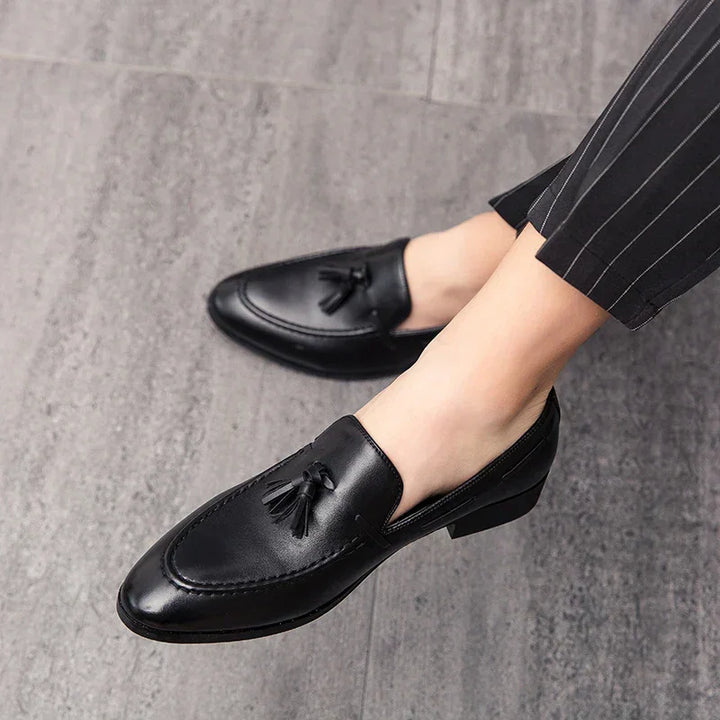 A person wearing mens loafers crafted from genuine leather and pinstripe pants, standing on a grey tiled floor.