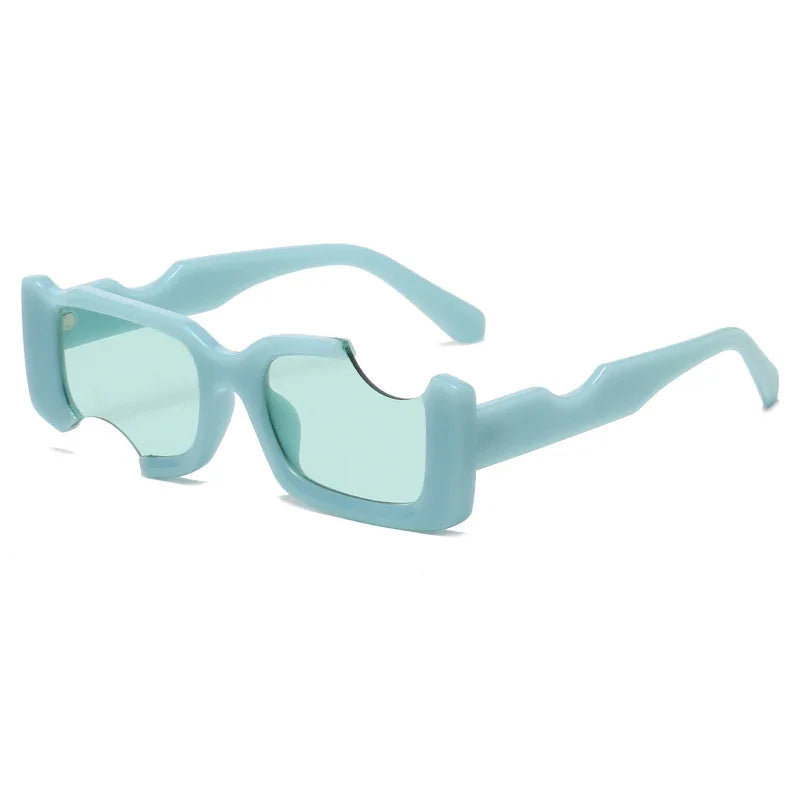 Light blue rectangular sunglasses with thick geometric frames and green-tinted lenses. Angular, wavy cutouts along the top edges and arms create a distinctive, futuristic design perfect for bold street style looks.