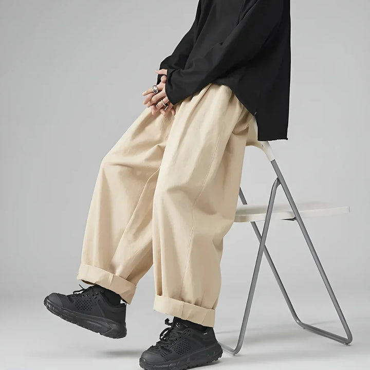 Model sits on chair in beige wide-leg pants, black shirt, and black sneakers, Rovelli style