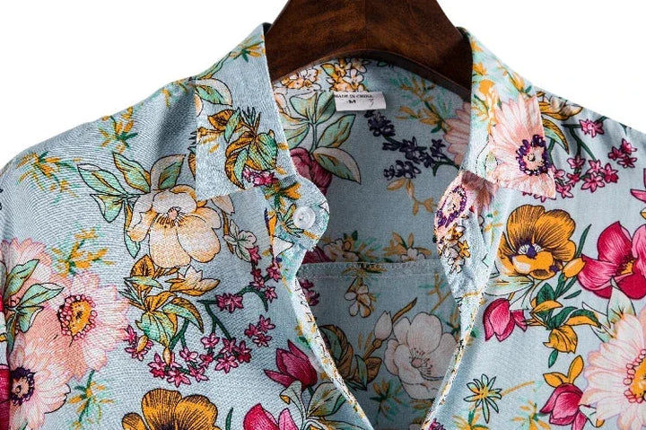 Close-up of a light blue floral shirt with pink, yellow, and orange flowers and green leaves, made from easy-care material, hanging on a wooden hanger.