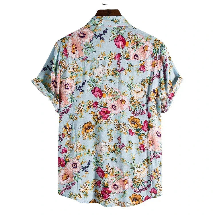 A vintage-inspired shirt, this light blue, short-sleeve button-up features a colorful floral pattern in pink, yellow, purple, and green. The lightweight linen shirt is shown on a hanger with the back facing forward.