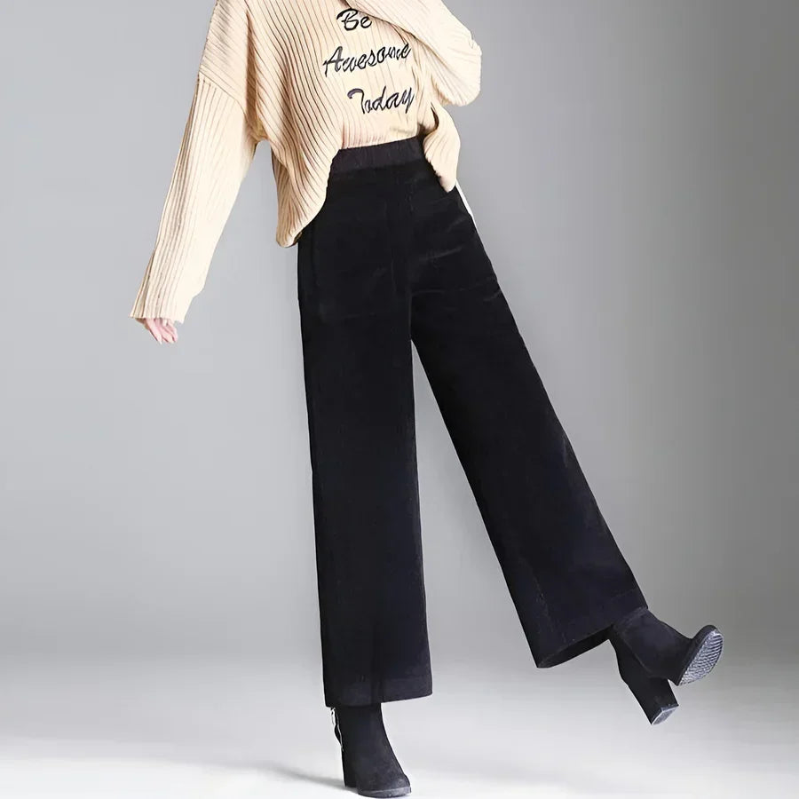 Woman wearing Rovelli wide-leg black pants and beige ribbed sweater, gray background