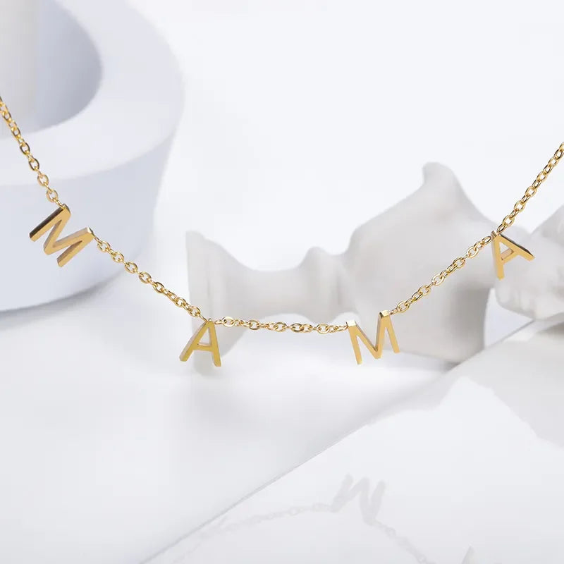 A gold minimalist jewelry piece, this stainless steel necklace features four dangling letter charms spelling MAMA, displayed against a white background with abstract white shapes.