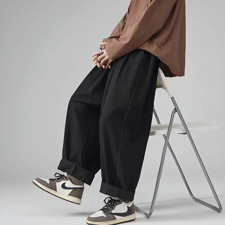 Rovelli model in wide leg black pants, brown shirt, and sneakers sitting on chair
