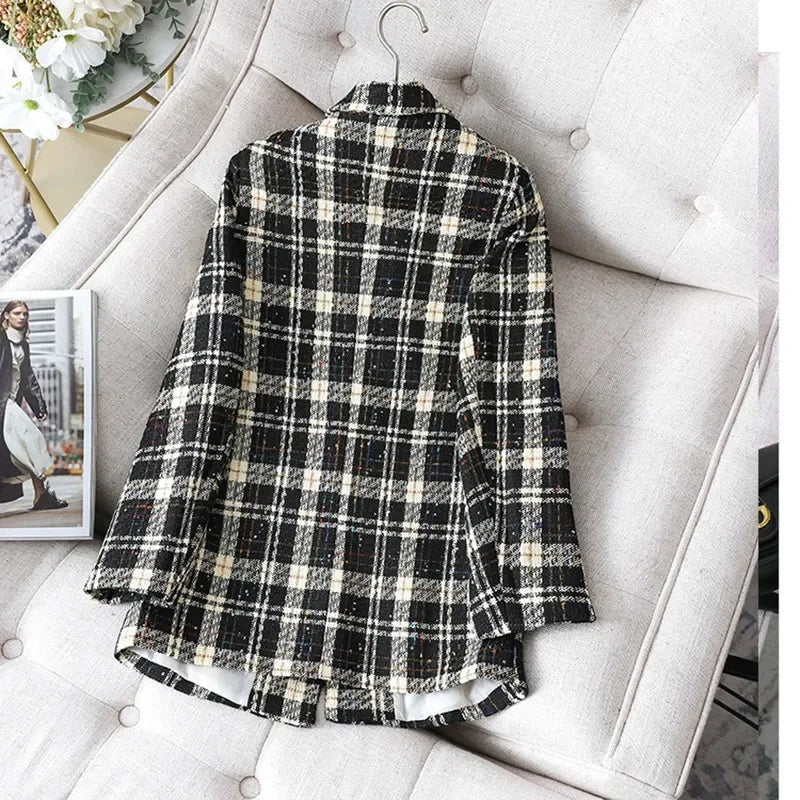 A black and white plaid formal blazer, perfect as an office work suit or stylish jacket coat, is displayed on a light-colored cushioned sofa with a hanger at the collar. A magazine and part of a bouquet are visible nearby.