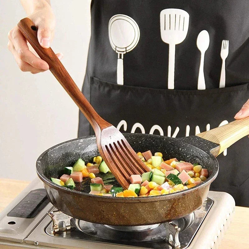 Person cooking vegetables and ham in a frying pan with a wooden spatula, wearing a black cooking apron, Rovelli kitchenware.
