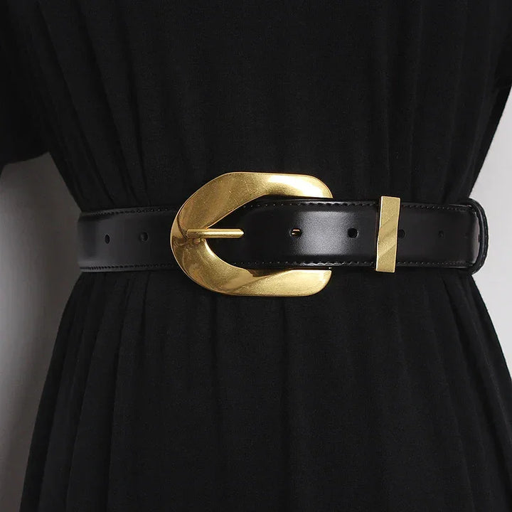A black dress is cinched at the waist with an adjustable belt featuring a large, shiny, gold oval buckle and gold details.