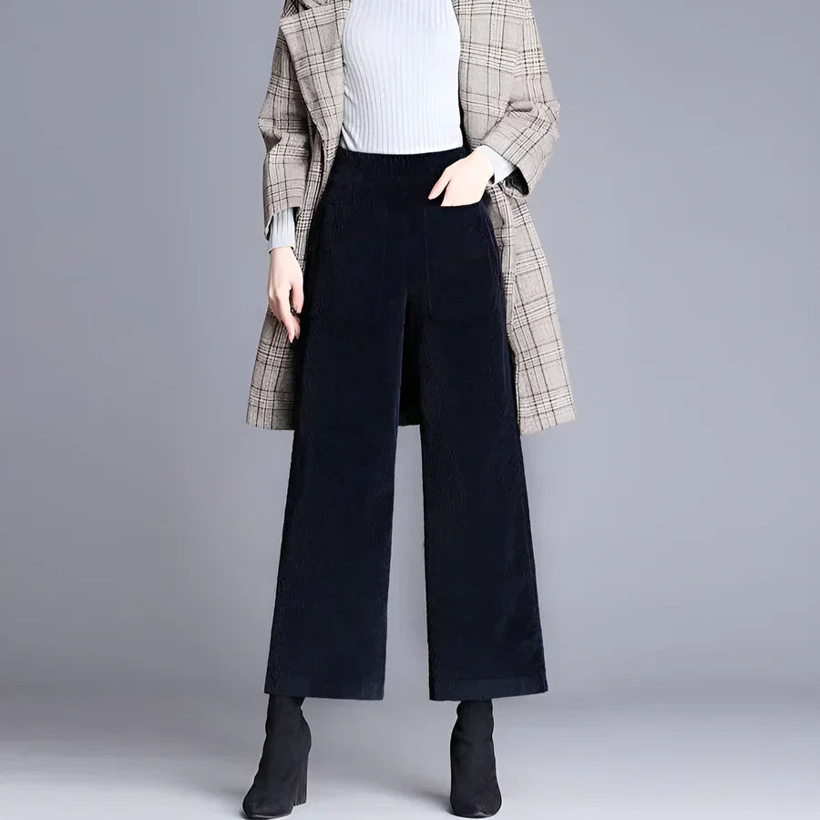 Woman wearing wide-leg black corduroy pants, plaid coat, and black boots from Rovelli