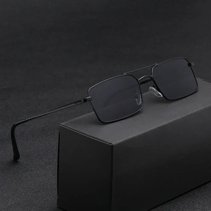 A pair of black rectangular sunglasses with thin, lightweight alloy frames rests on a black box, set against a dark, textured background.