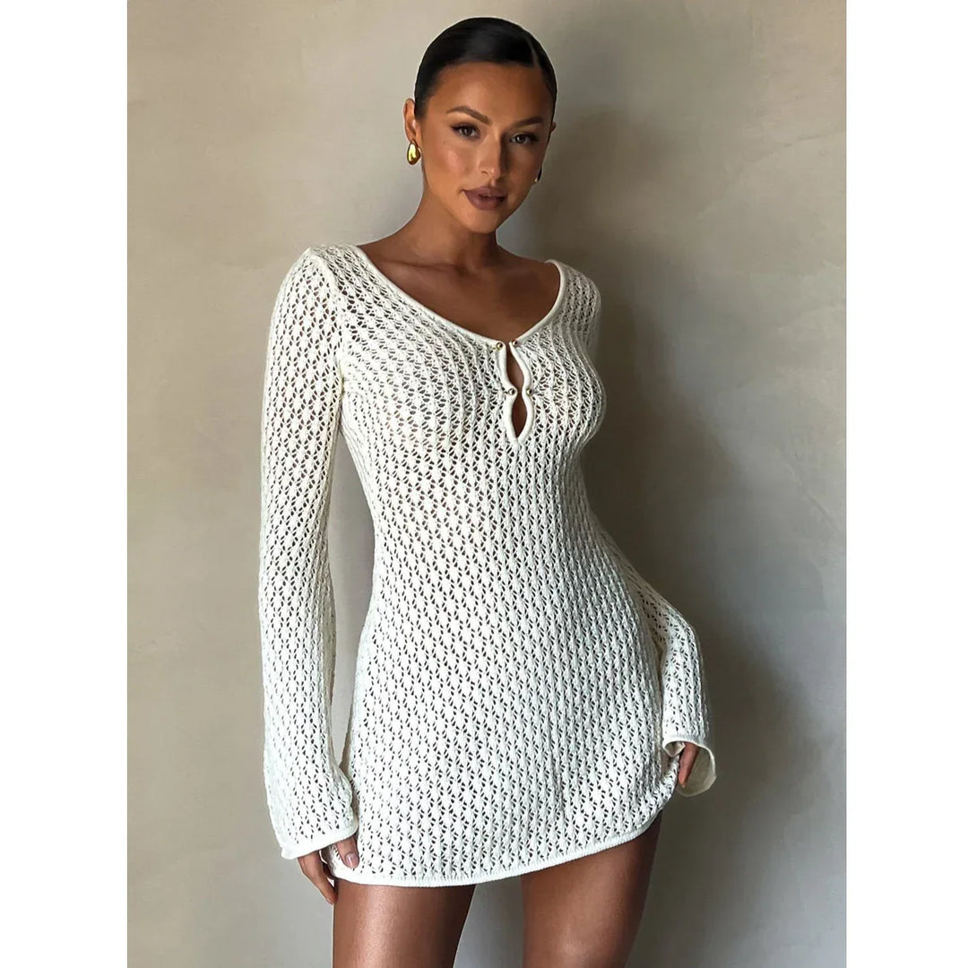 Woman wearing a white knit mini dress with long sleeves, posing against a beige wall, Rovelli fashion