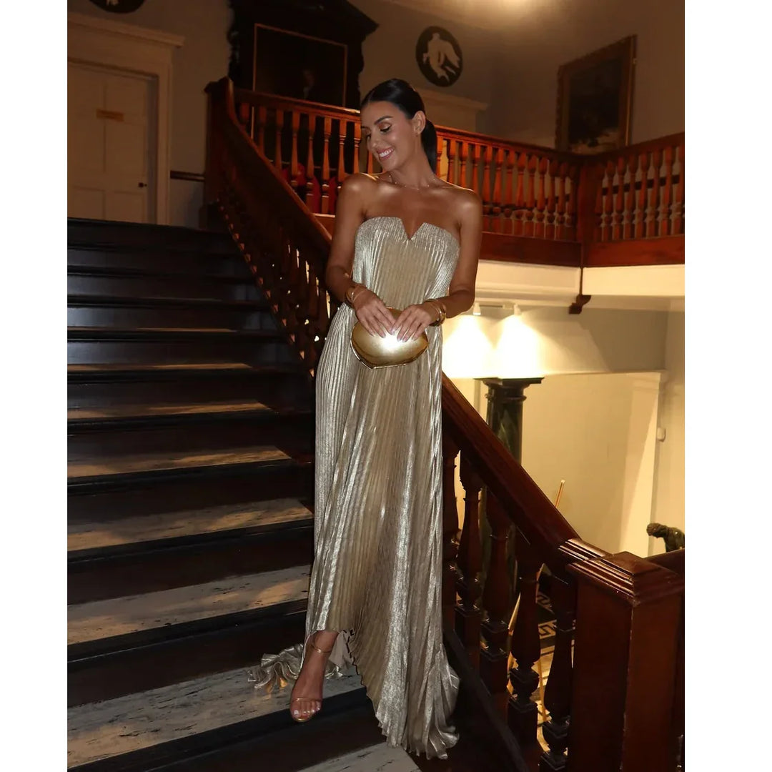 Woman in a metallic gold strapless dress holding a clutch on a grand staircase, Rovelli fashion