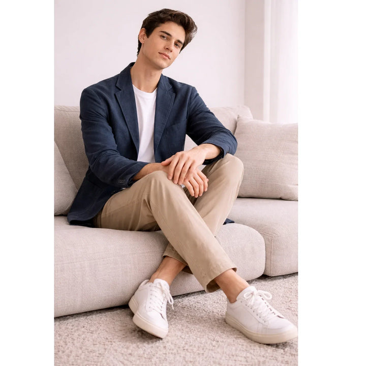 Man wearing navy summer blazer, khaki chinos, and white sneakers sitting on beige sofa