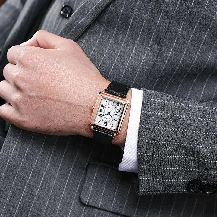 A person in a gray pinstripe suit and white shirt displays a luxury watch with Roman numerals on the face and a premium leather band.