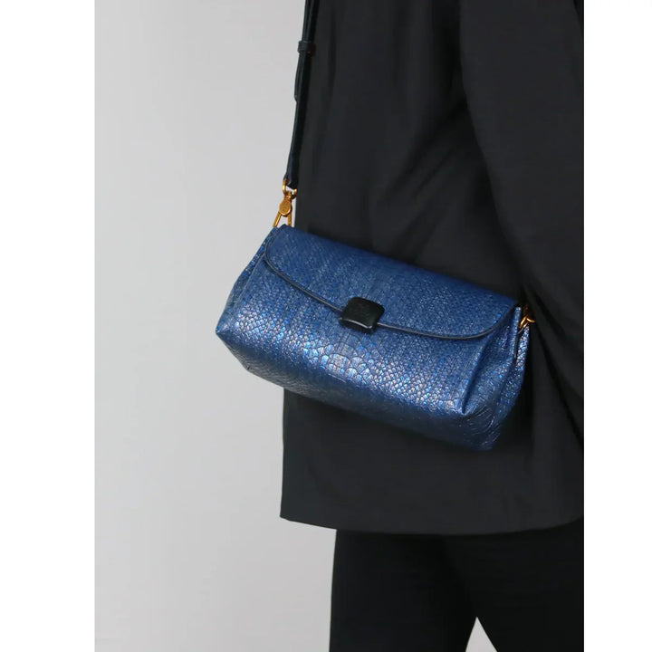 Rovelli blue textured crossbody shoulder bag with gold hardware, worn on black outfit