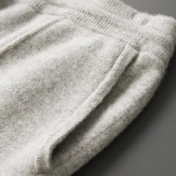 Close-up of a pair of light gray fleece sweatpants, highlighting the waistband, pocket, and soft, textured fabric on a dark background—crafted for durable construction and designed to be your most comfortable pants.