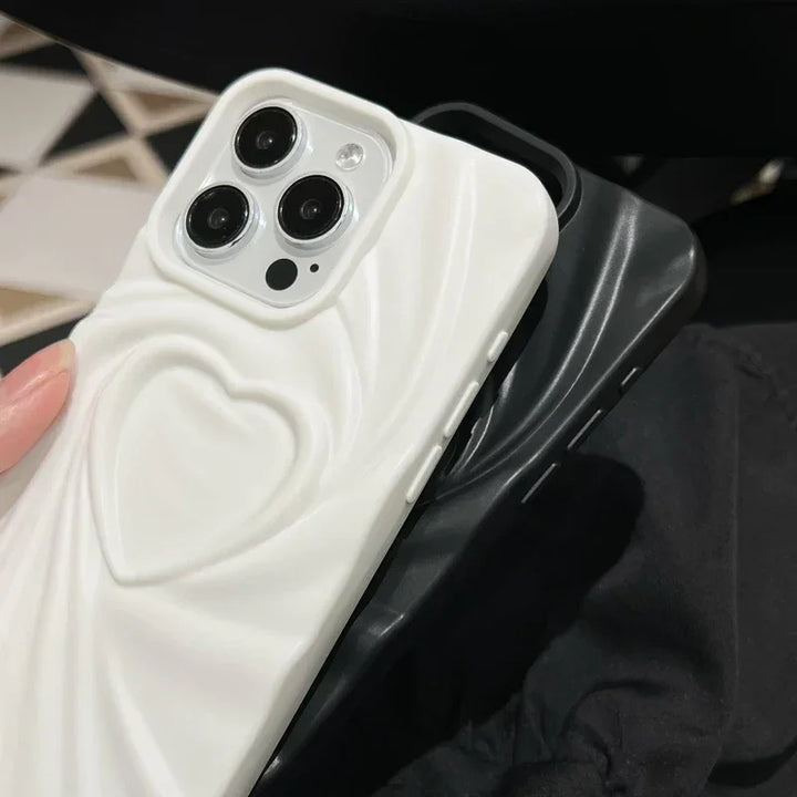 Two smartphones with full coverage protection: one features a white soft matte silicone case with a 3D heart design, while the other boasts a black case with a smooth, wavy pattern. Both are held close together against a dark background.