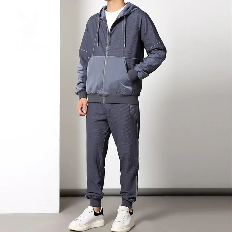 A person wearing a gray activewear set, featuring a zipper hoodie with matching jogger pants and white sneakers, stands against a plain white and gray background. The hands are relaxed at the sides, and the head is not visible.